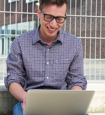 Portrait of a happy student working on laptop outdoors