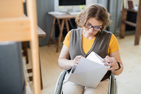 Young secretary or accountant in wheelchair looking through financial papers